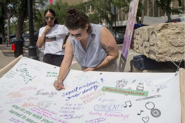 People writing on a banner why sex-ed is important