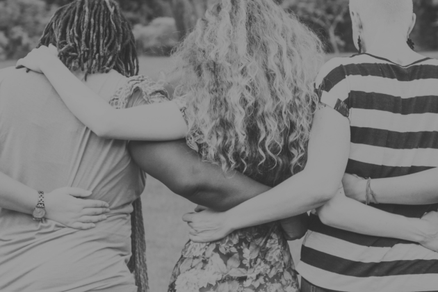 Black and white photo of a five people facing away from the camera, in a linear embrace