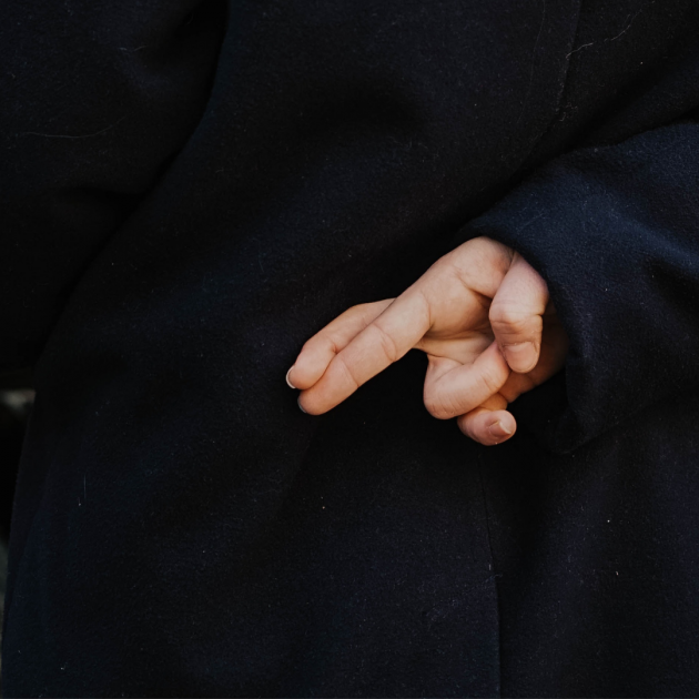 Close crop of a person crossing their fingers behind their back